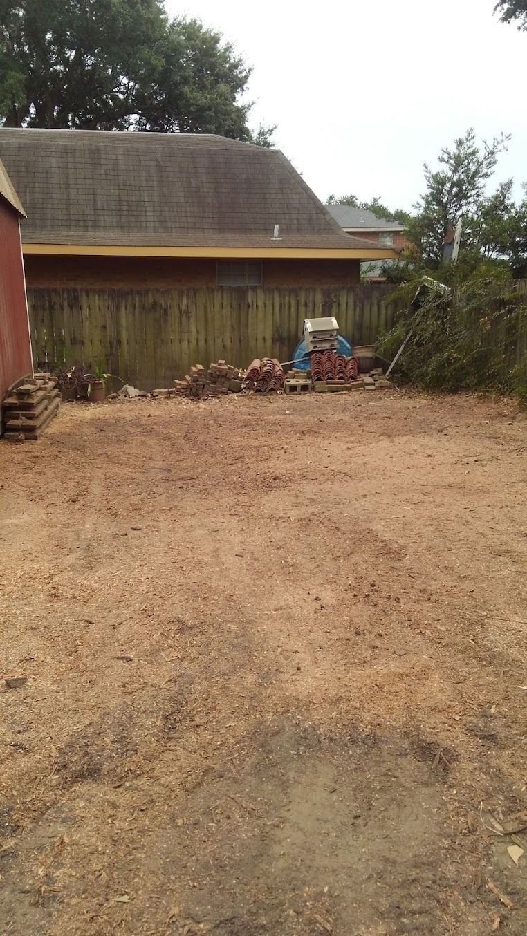 Gravel driveway leading to a rustic wooden house with a thatched roof and scattered yard items.