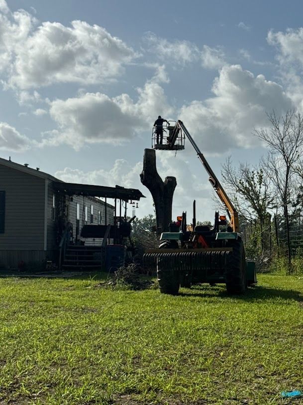 Workers use a crane to lift a large dark object beside a house under a cloudy sky.