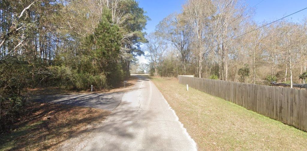 Quiet paved path through a wooded park beside a wooden fence on a sunny day