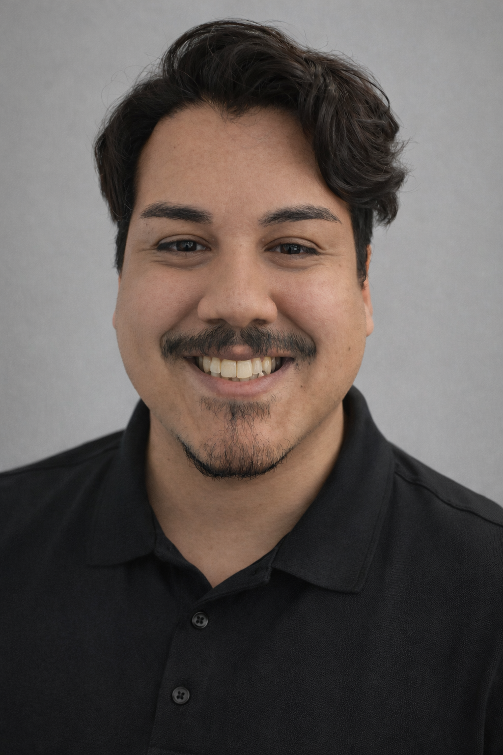 A young man with a beard and mustache is smiling for the camera.