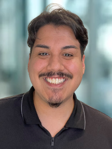 A young man with a beard and mustache is smiling for the camera.