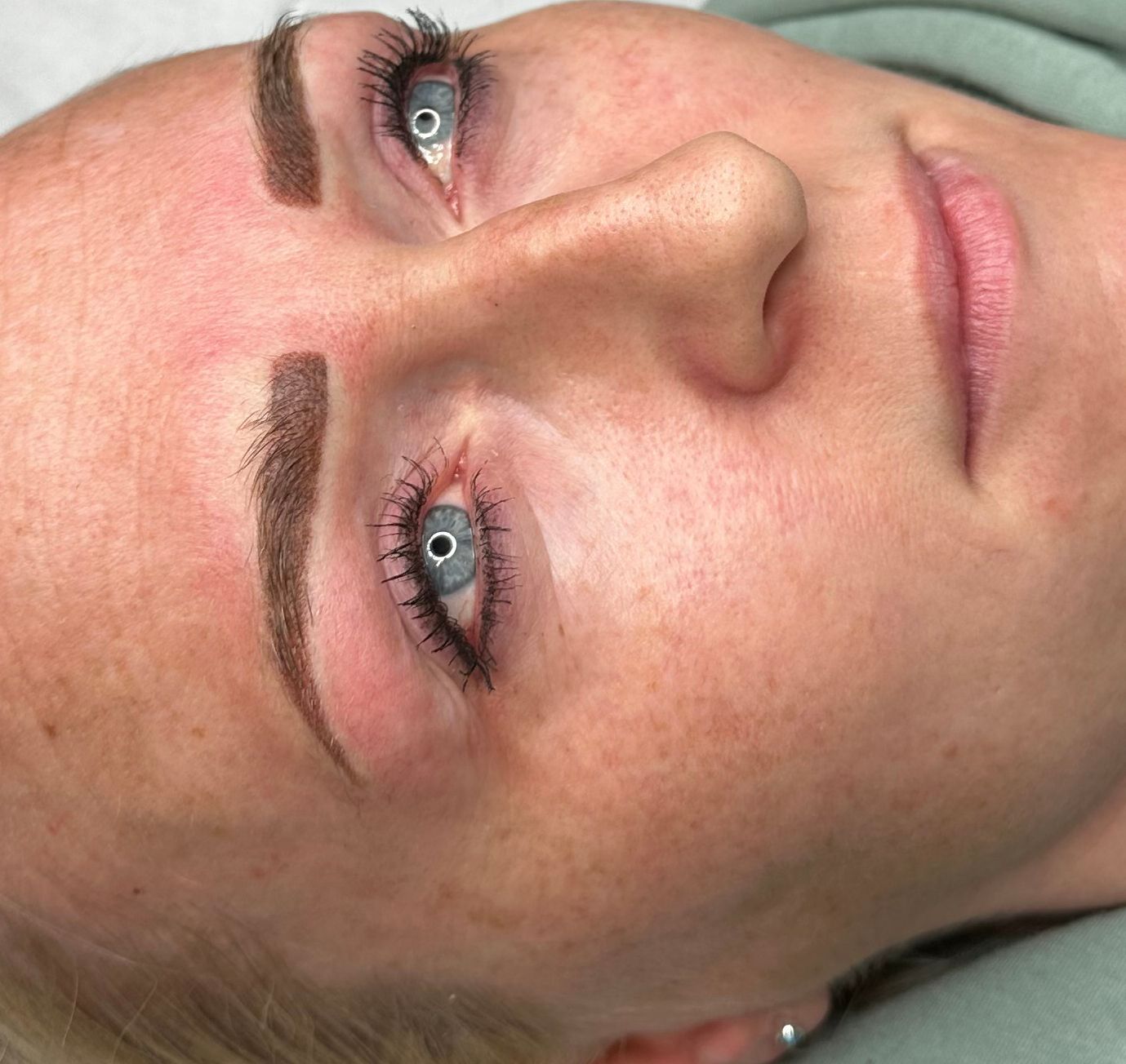 Woman's face close-up, focusing on professionally styled eyebrows and eye makeup. Light skin, blue eyes, neutral expression.