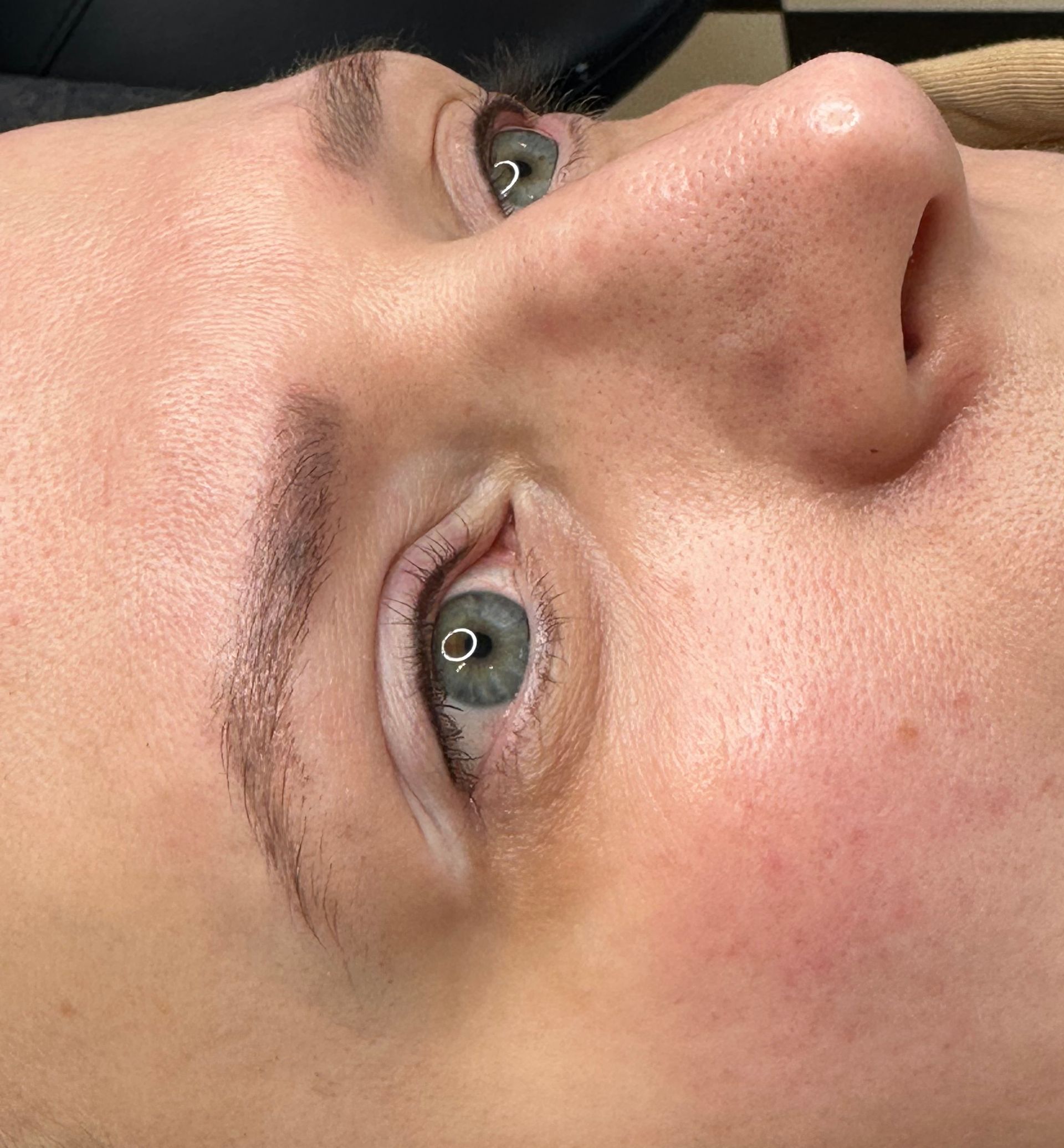 Close-up of a person's eye and eyebrow with permanent makeup. The skin is light, eyes are blue-green.
