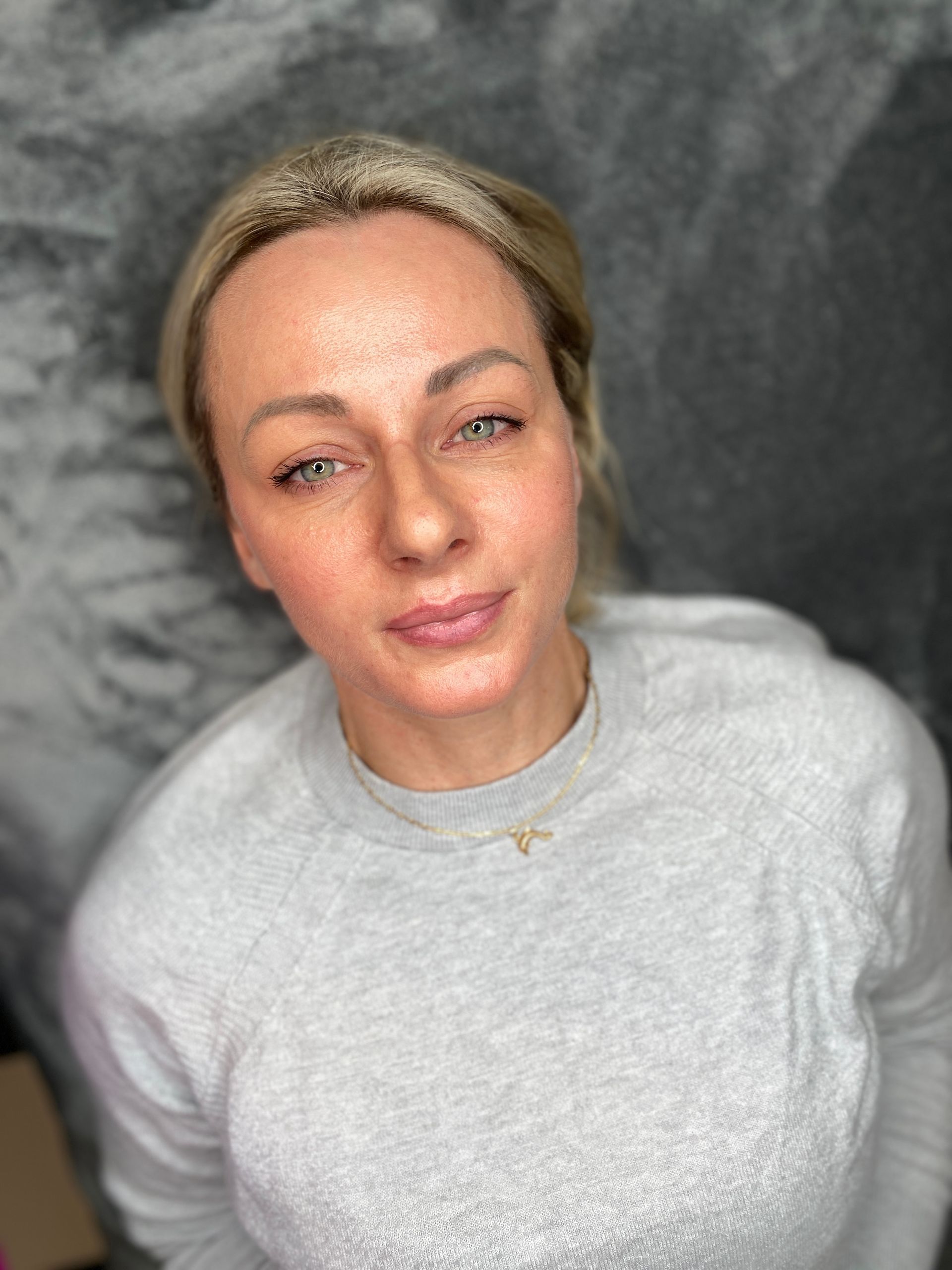 Woman with blonde hair wearing a gray sweatshirt, gazing at the camera.