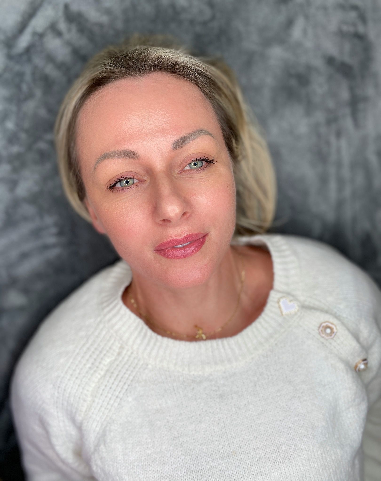 Woman in white sweater looks up, hair back, on grey background.