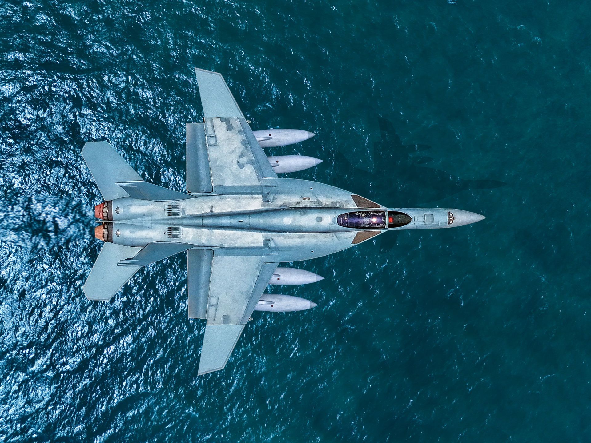 An aerial view of a fighter jet flying over the ocean.