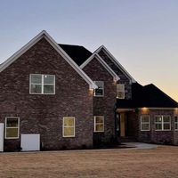 Brick house with white trim, multiple windows, and a dark roof under a dusky sky.
