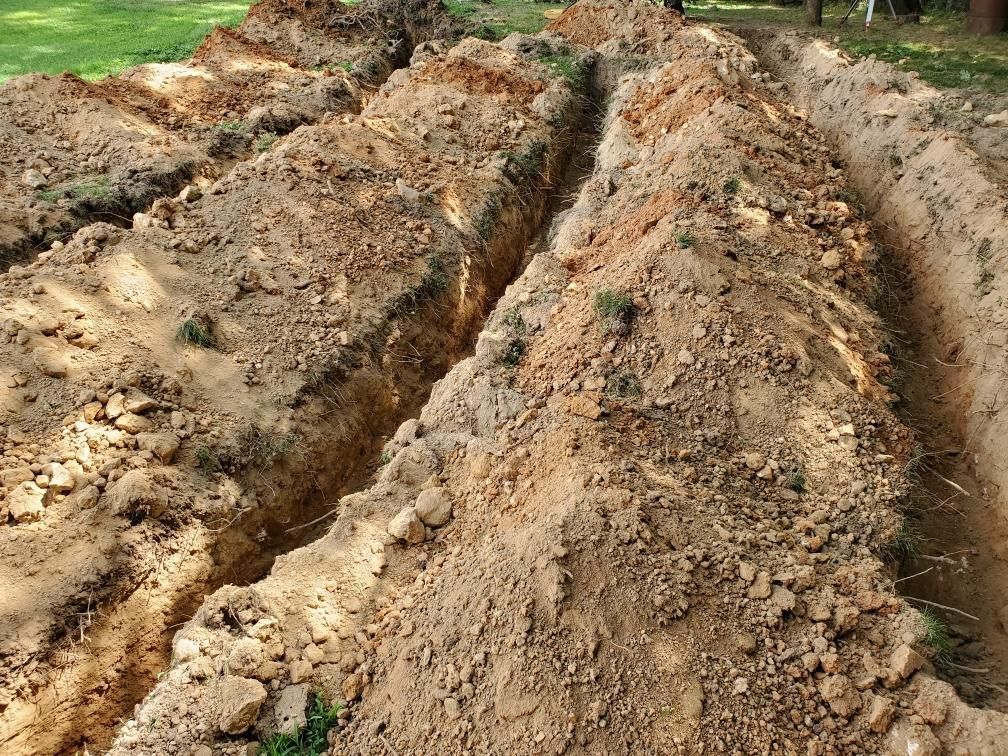 Deep muddy trenches cut through a dirt field, with grass along the edges.