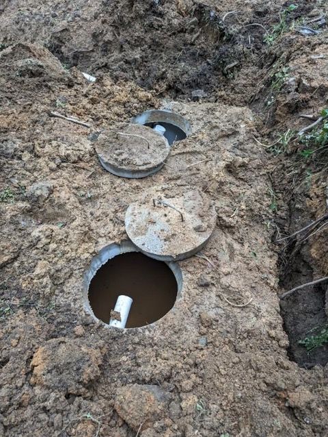 Two open circular utility access holes in muddy ground, with round lids nearby.