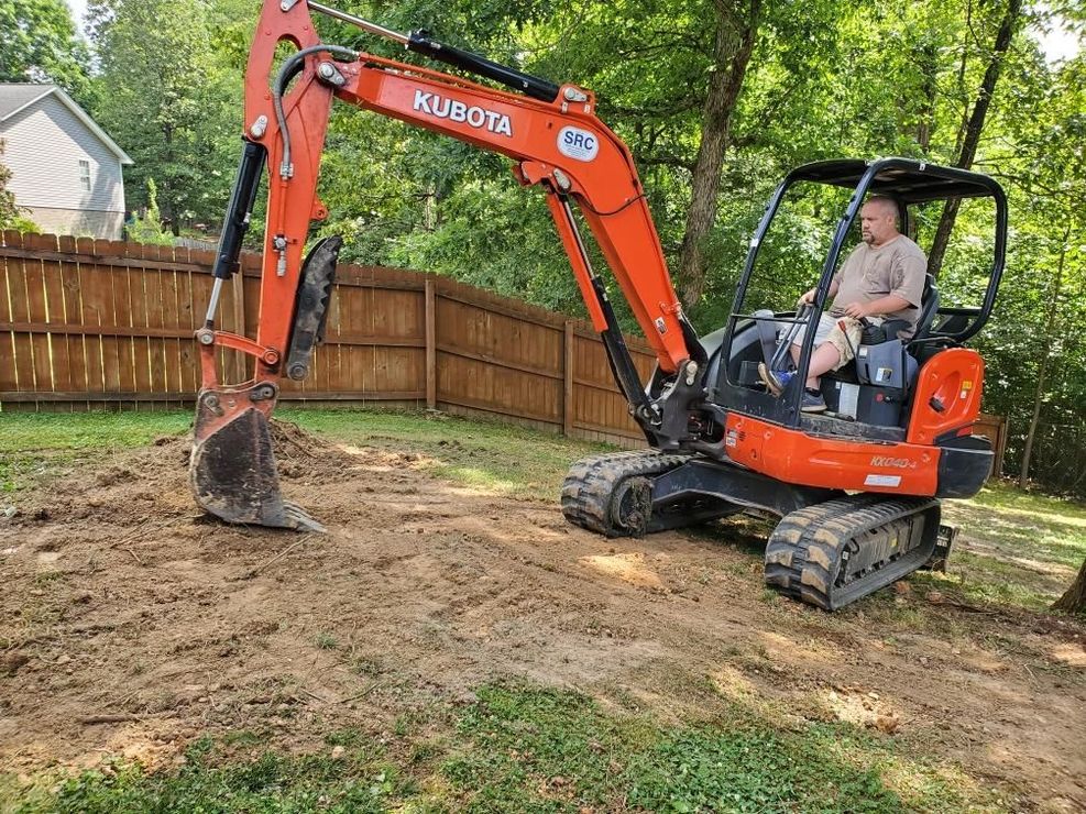 Orange Kubota excavator digging dirt in a backyard beside a wooden fence and house