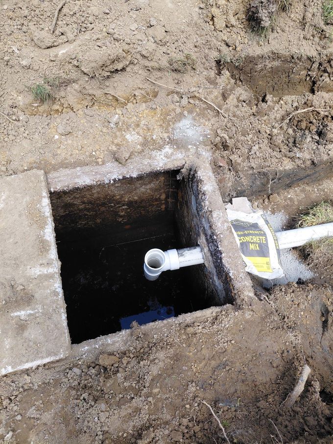 Open ground utility pit with a pipe and exposed soil around the opening.