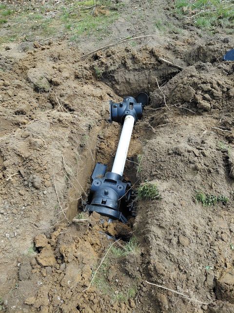Field line connection in a dirt trench, with a white pipe between two black fittings.