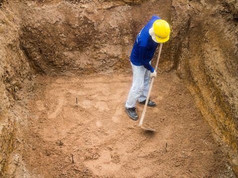 Worker in a hard hat digging a dirt excavation pit with a shovel