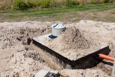 Concrete utility box in a sandy excavation with orange pipes and a grassy background