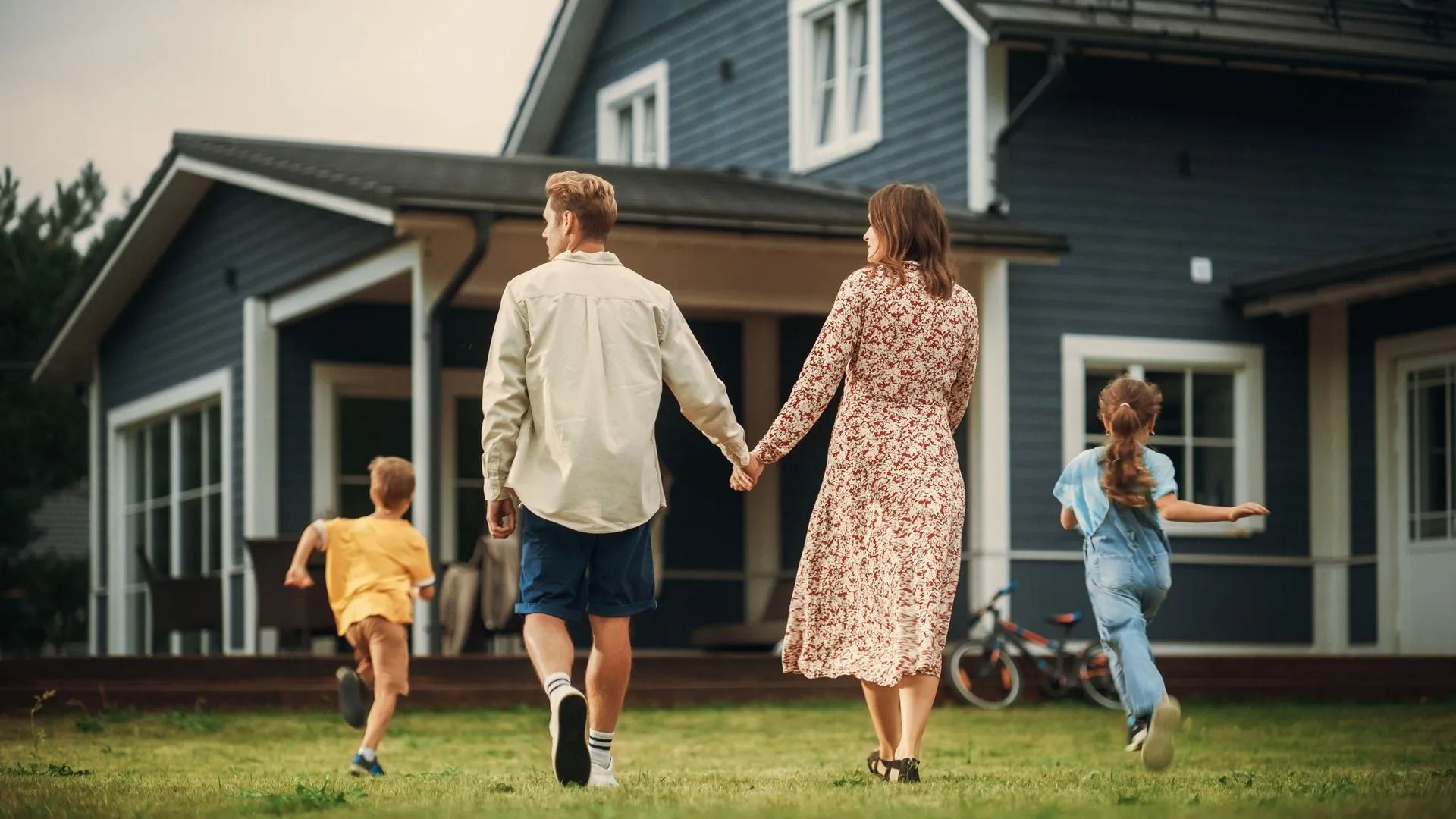 Family holding hands and walking toward a dark blue house across the lawn
