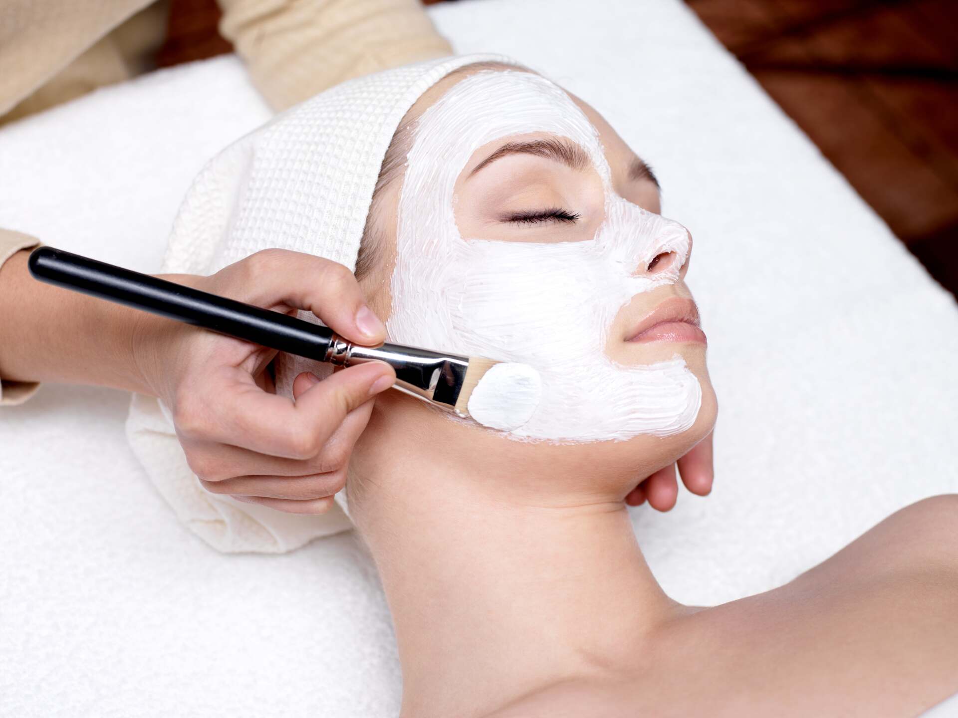 beautician-with-brush-applies-white-moisturizing-mask-face