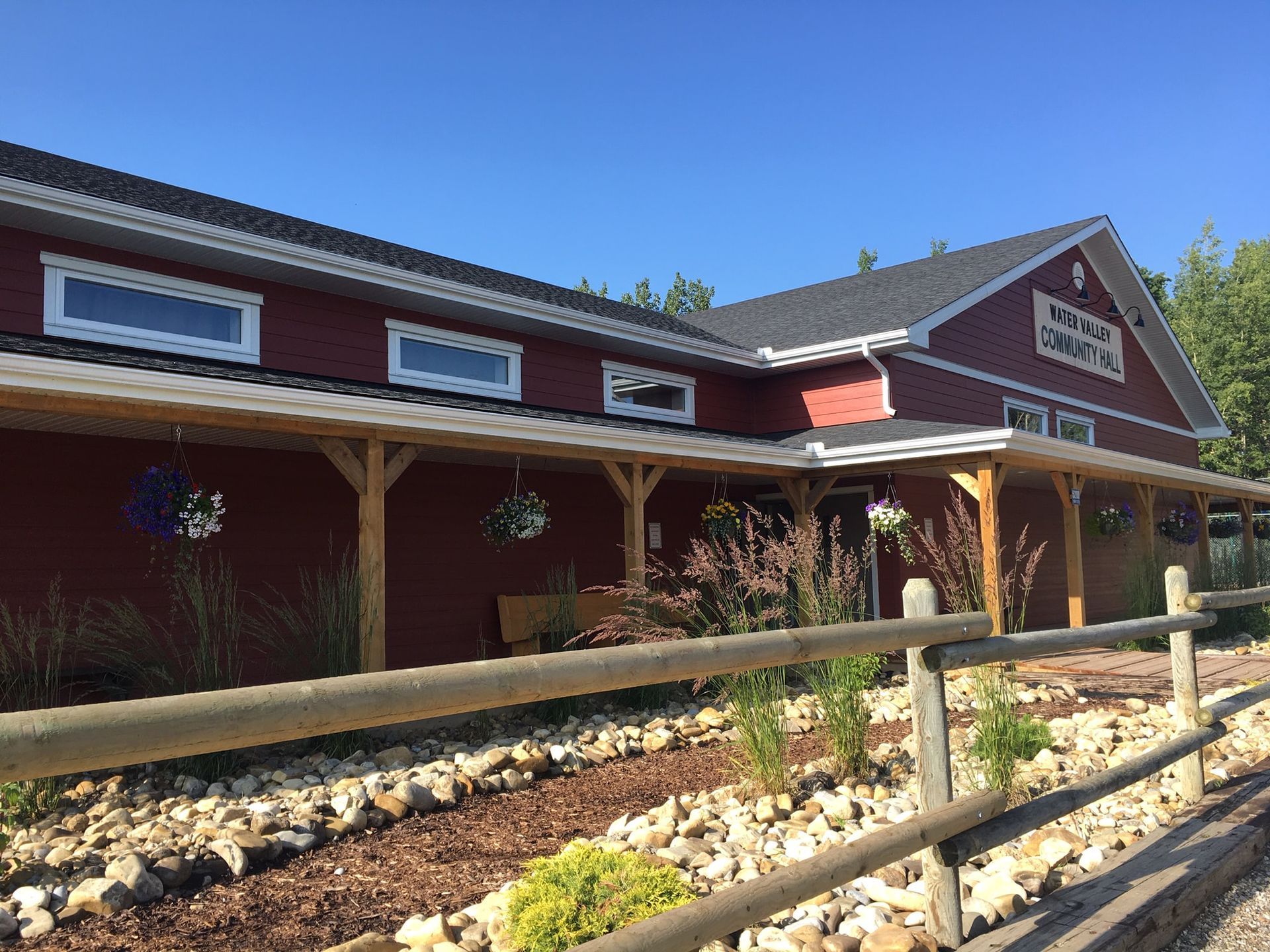 Red building with a wooden porch and a split-rail fence in the foreground, under a clear blue sky.
