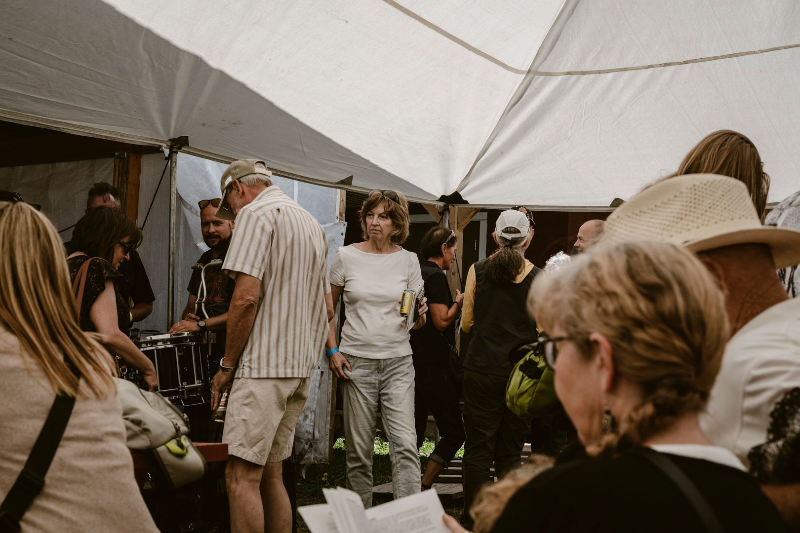 A crowd of people stands under a large white tent, with some interacting and others looking toward an event or speaker.