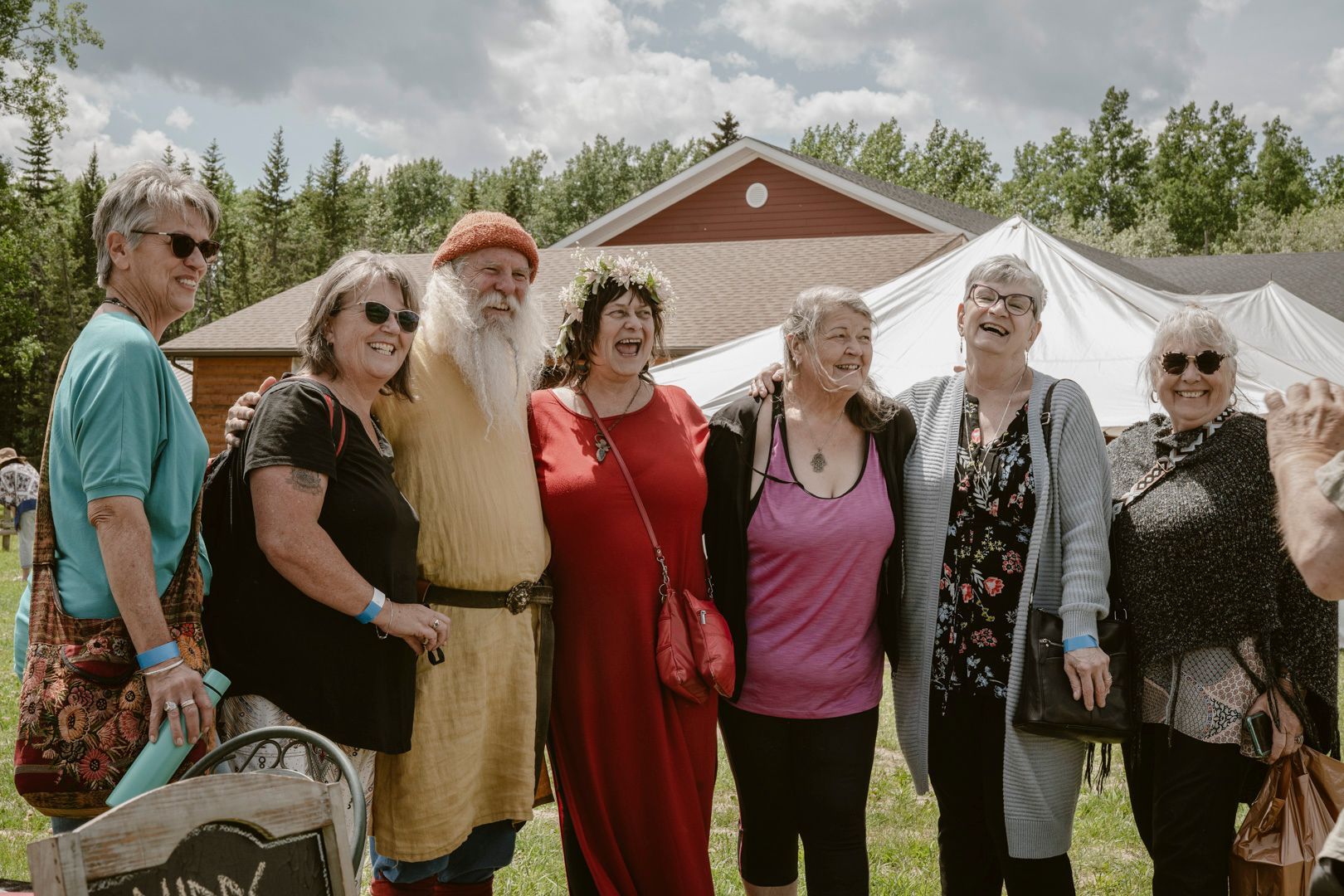 A group of people standing together outdoors, smiling and laughing during a sunny daytime event near a building and tent.