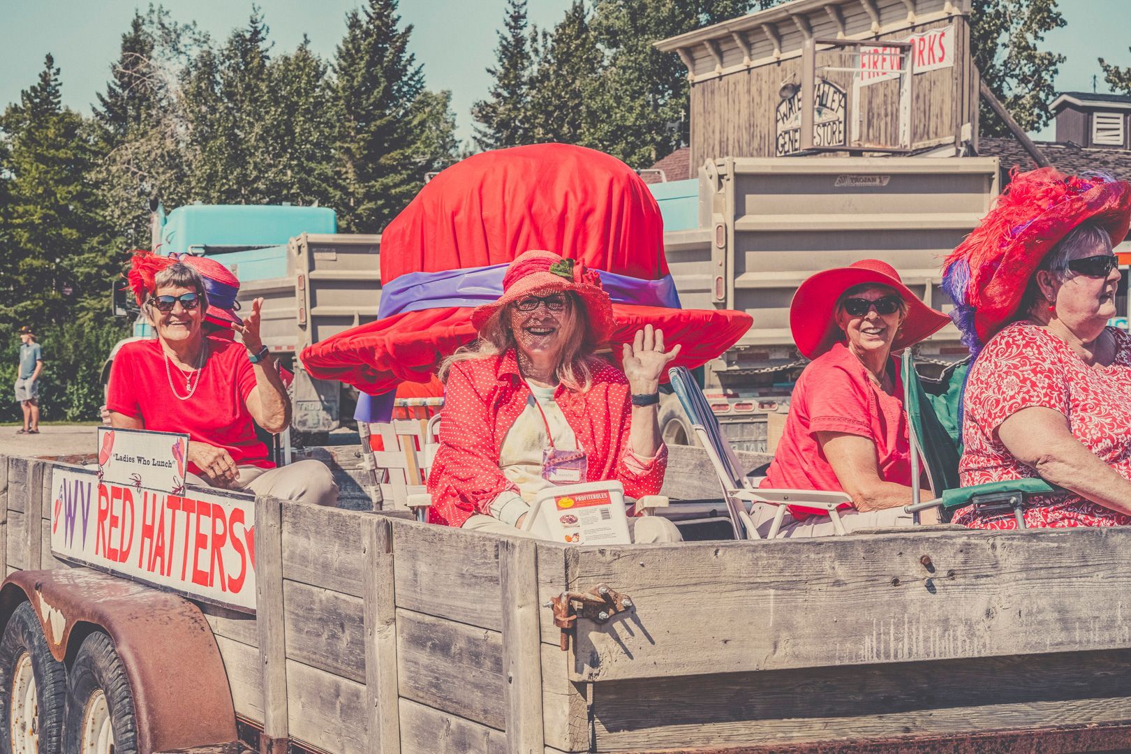 Four people in red outfits and large red hats ride on a flatbed trailer labeled 