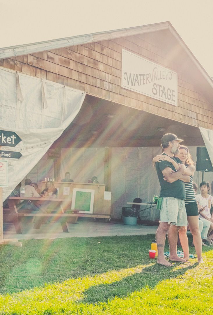 A couple embraces outside a wooden shelter labeled 