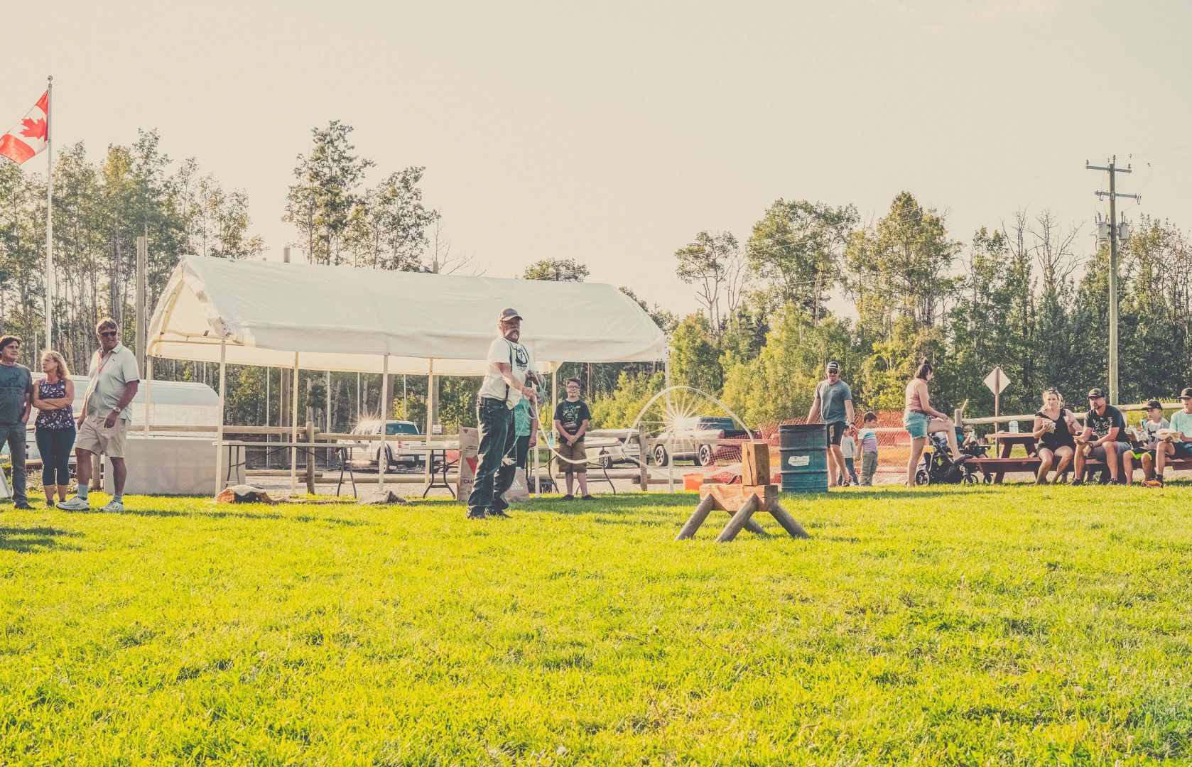 A person throwing a baton at wooden blocks in a grassy field during an outdoor event with spectators.
