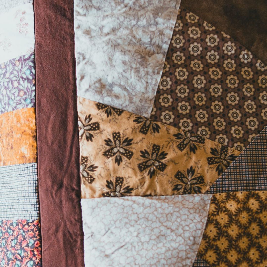 A patchwork quilt made of various fabric patterns in shades of brown, beige, and orange, featuring geometric shapes.
