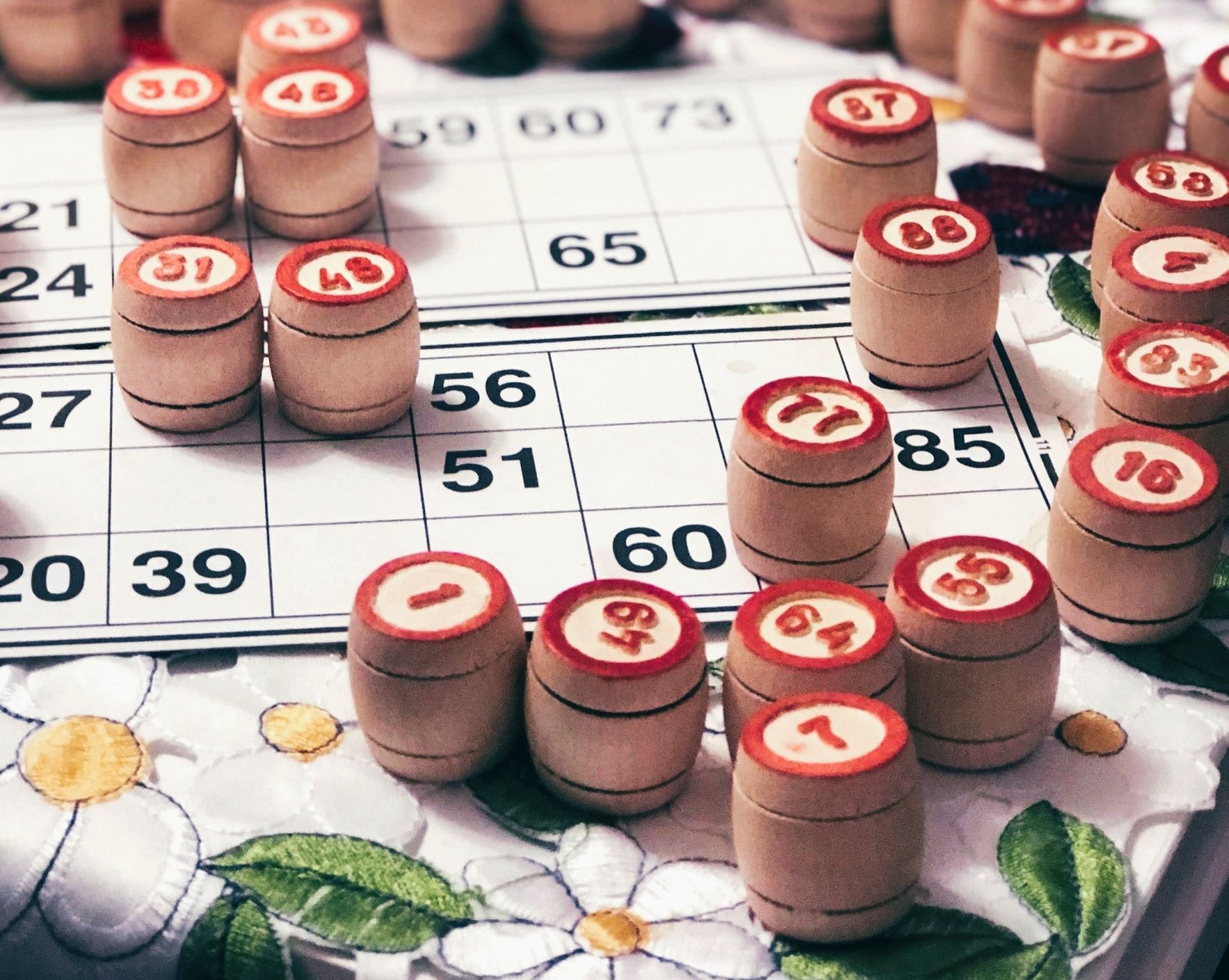 A close-up of wooden numbered bingo barrels scattered on a patterned floral surface over a game board.
