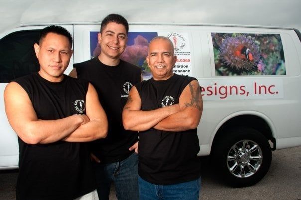 Three men standing in front of a van that says signs inc.