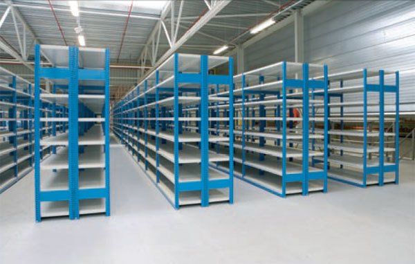 Rijen lege industriële metalen stellingen met witte schappen en blauwe frames in een felverlicht magazijn.