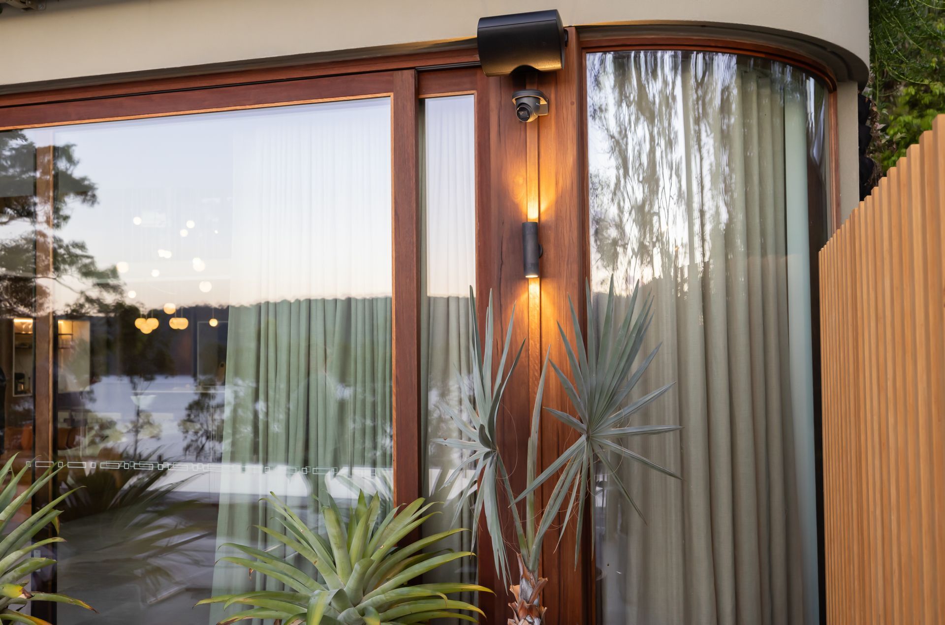 Modern house exterior with large glass windows, wood siding, and tall desert plants at dusk