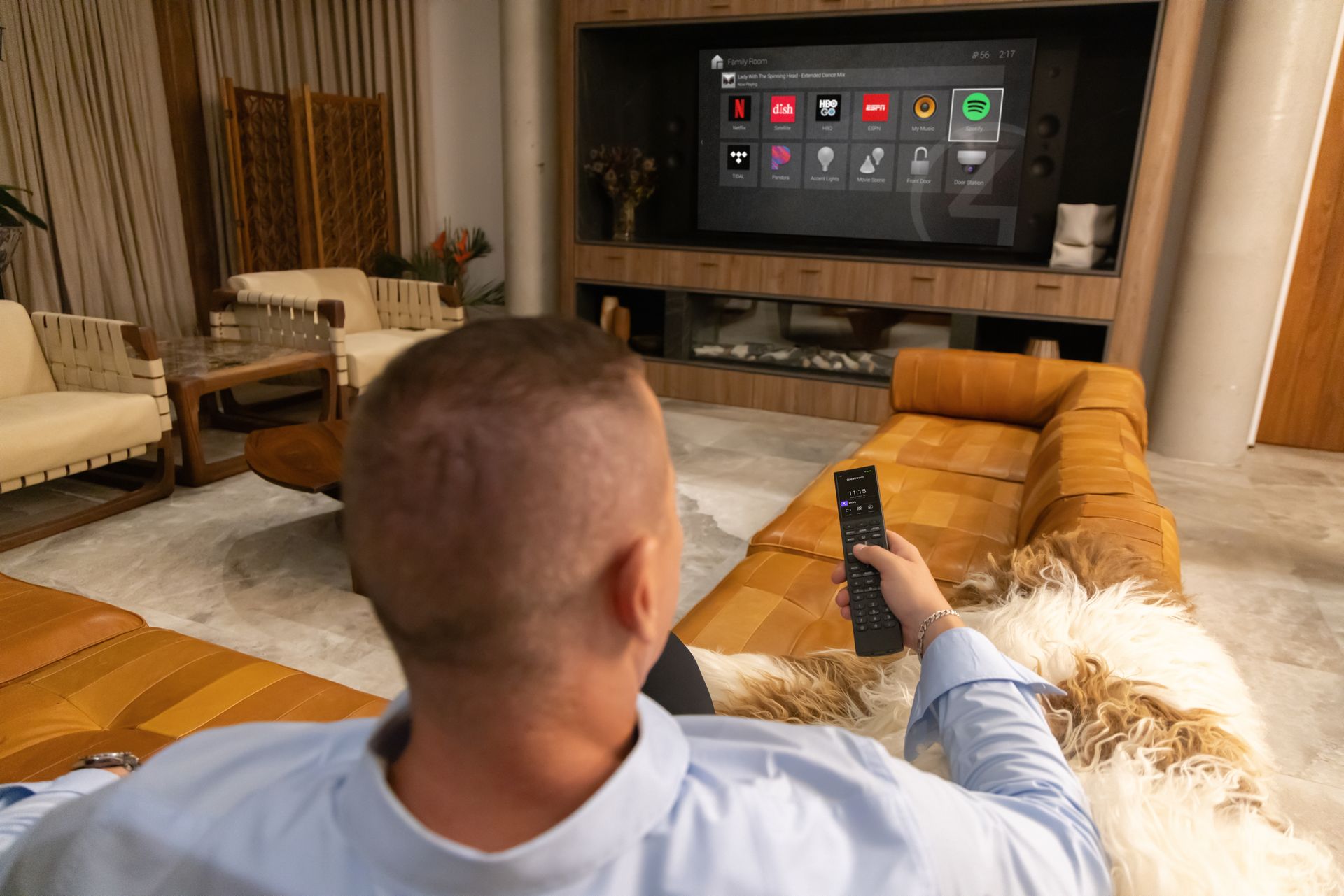 Person sitting on a couch pointing a remote at a TV in a modern living room.