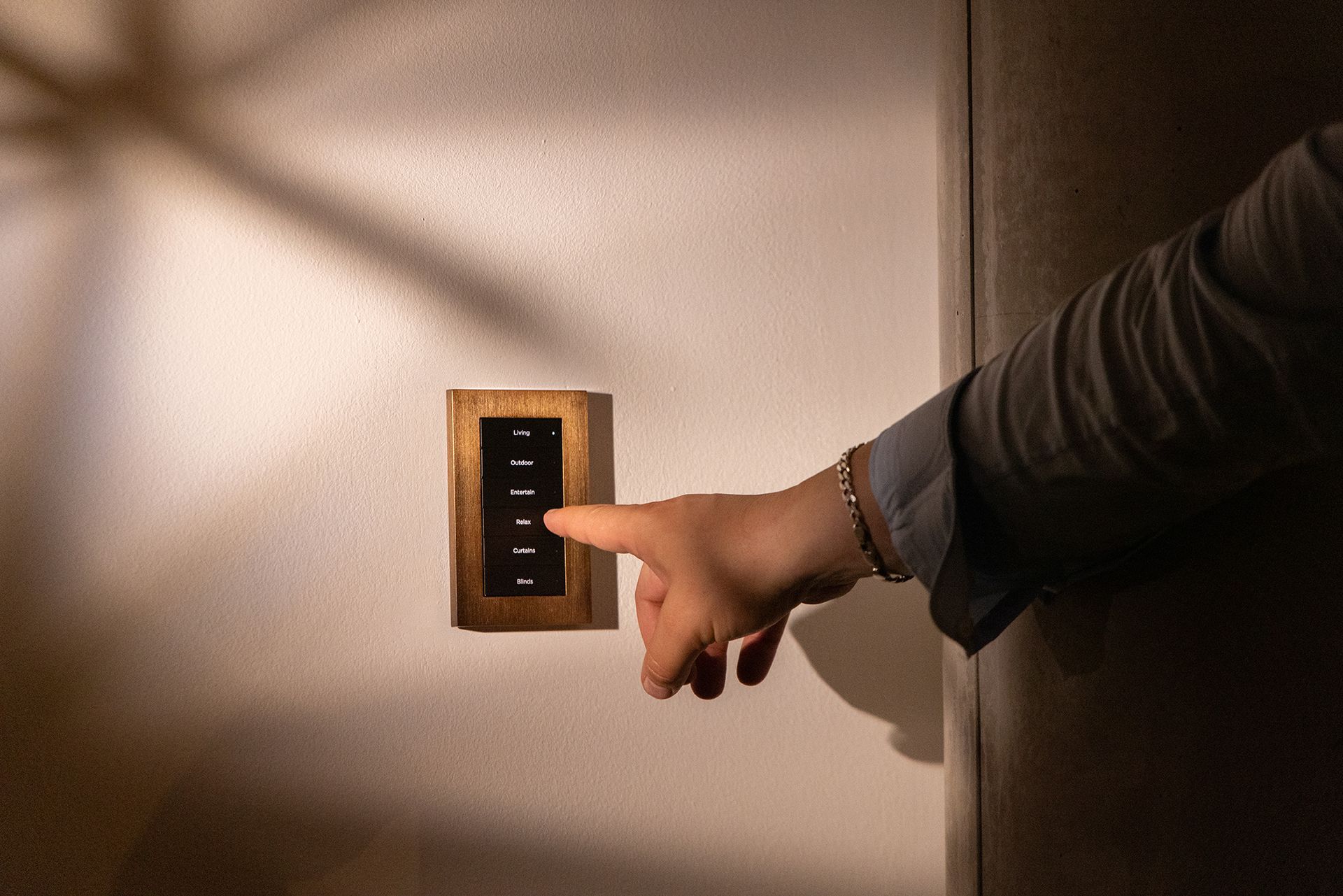 Hand pressing a wall-mounted light switch panel in a dim room
