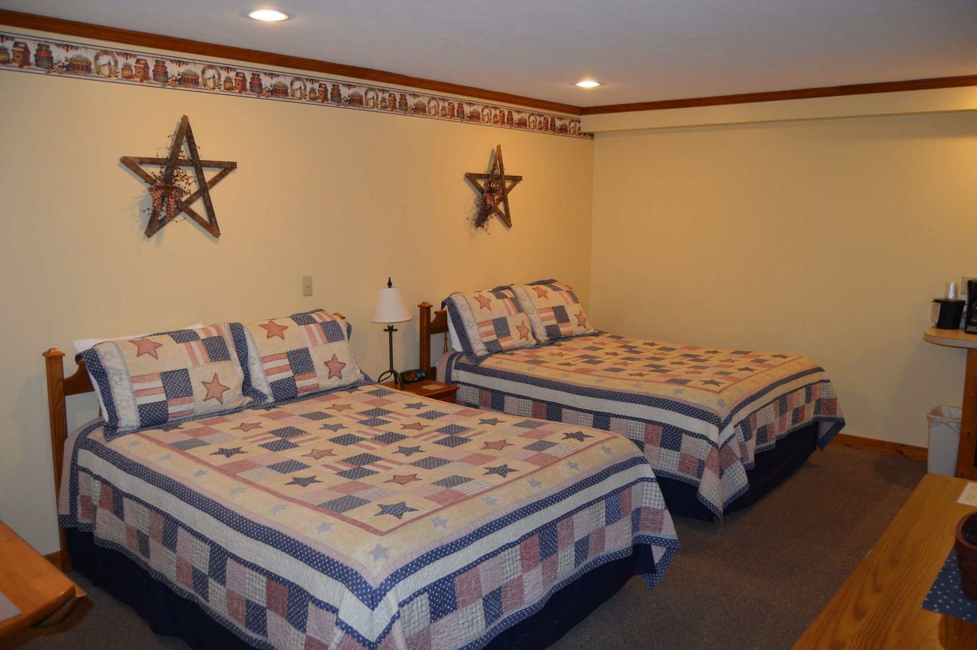 Two neatly made twin beds with patchwork quilts in a cozy beige bedroom with star wall decor.