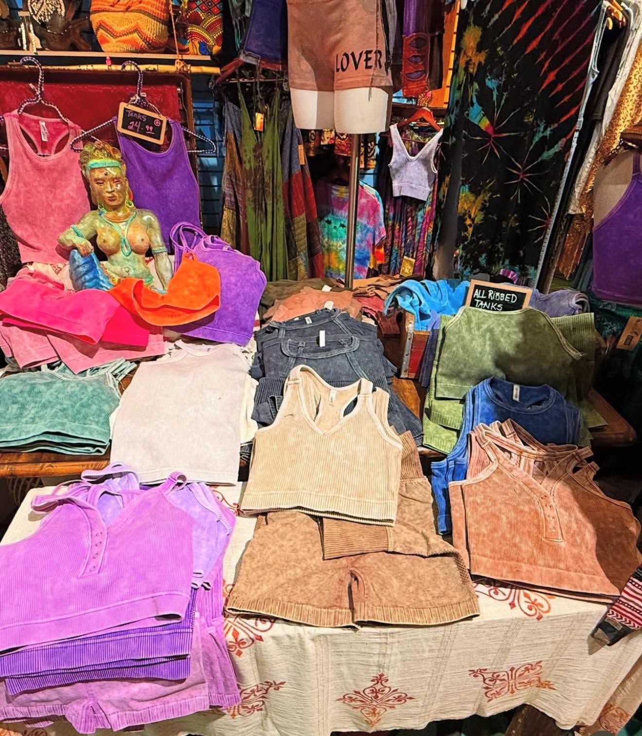 Clothing stall with folded tops and skirts in pastel and earth tones, plus a small Buddha statue on the left.