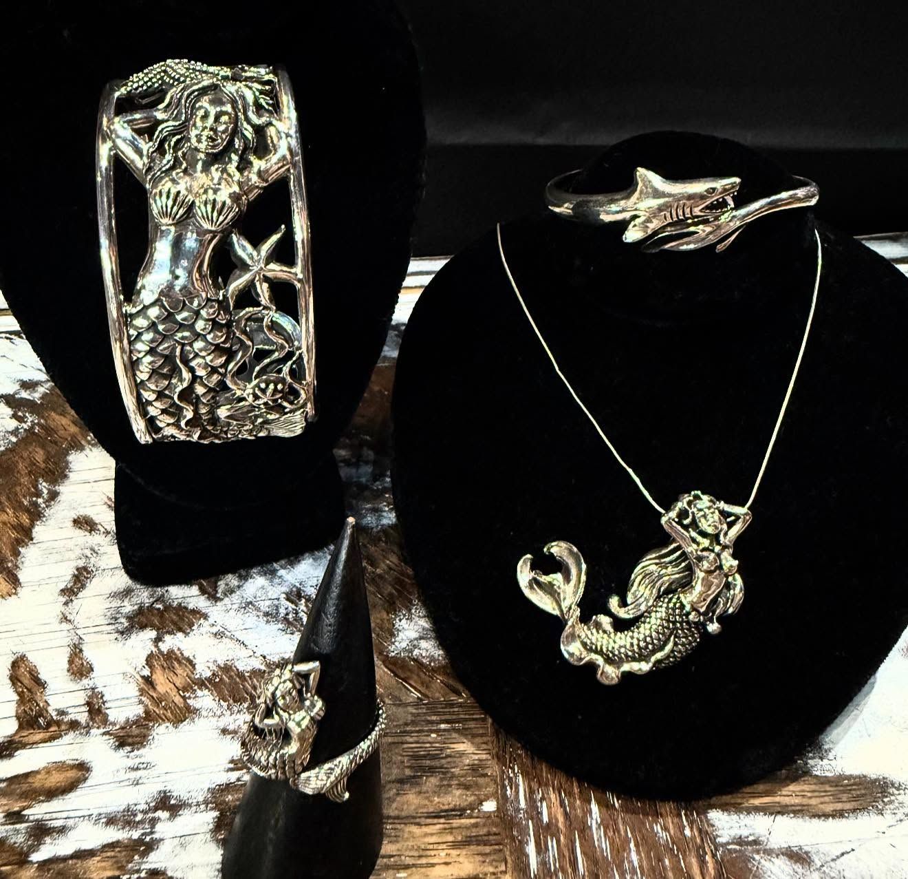 Silver jewelry display on black velvet stands, featuring a pendant necklace, cuff bracelet, and ring.