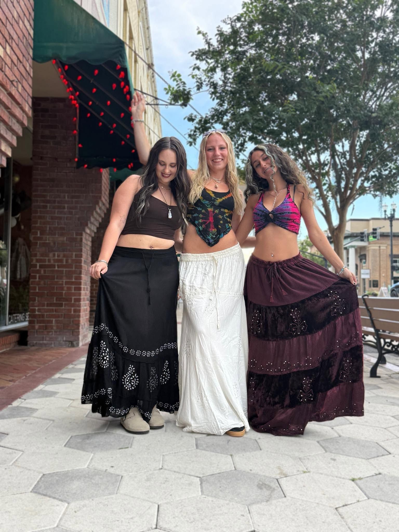 Three people posing outdoors in colorful outfits on a sidewalk.