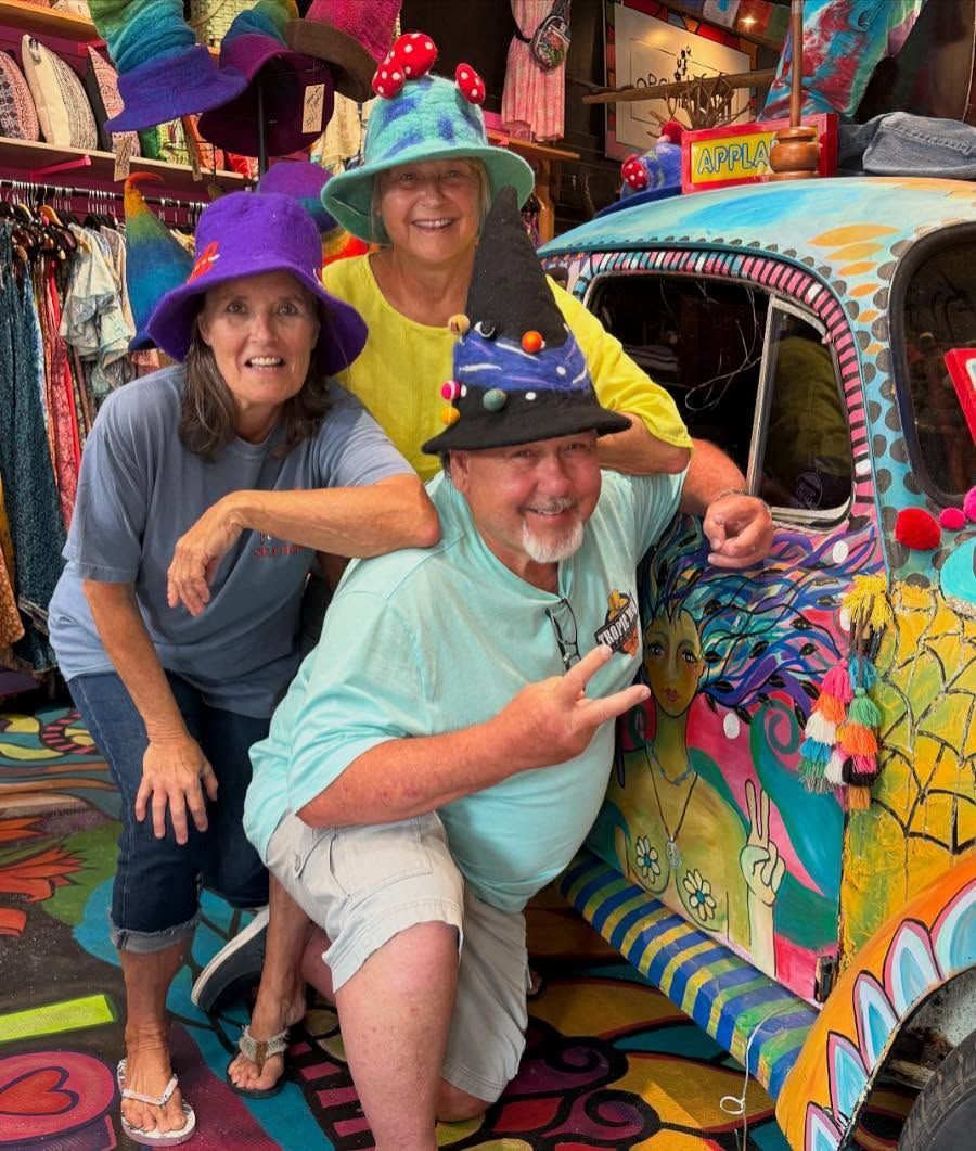 Three people posing beside a brightly painted, decorated car in a colorful setting