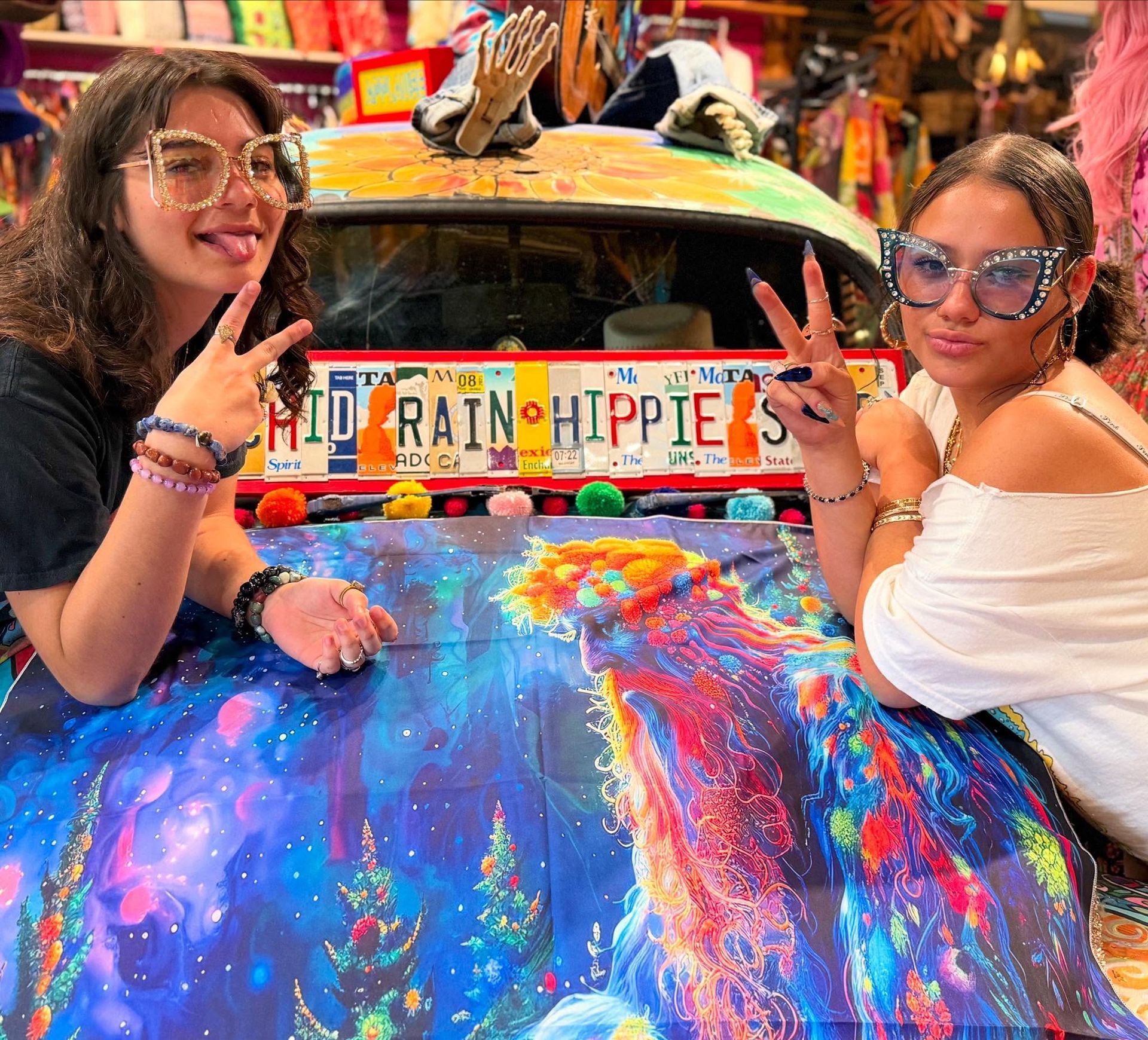 Two women pose beside a colorful painted van with “RAINBOW PIPES” on the front.