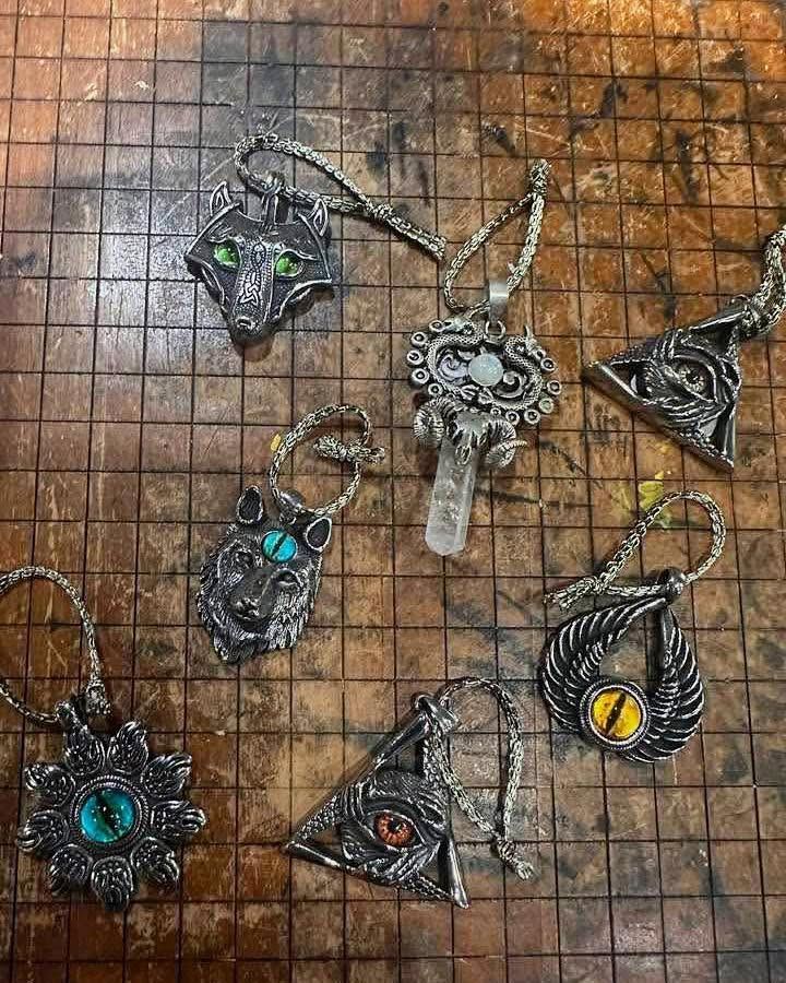 Five ornate metal pendants with colored gemstones on a wire grid background