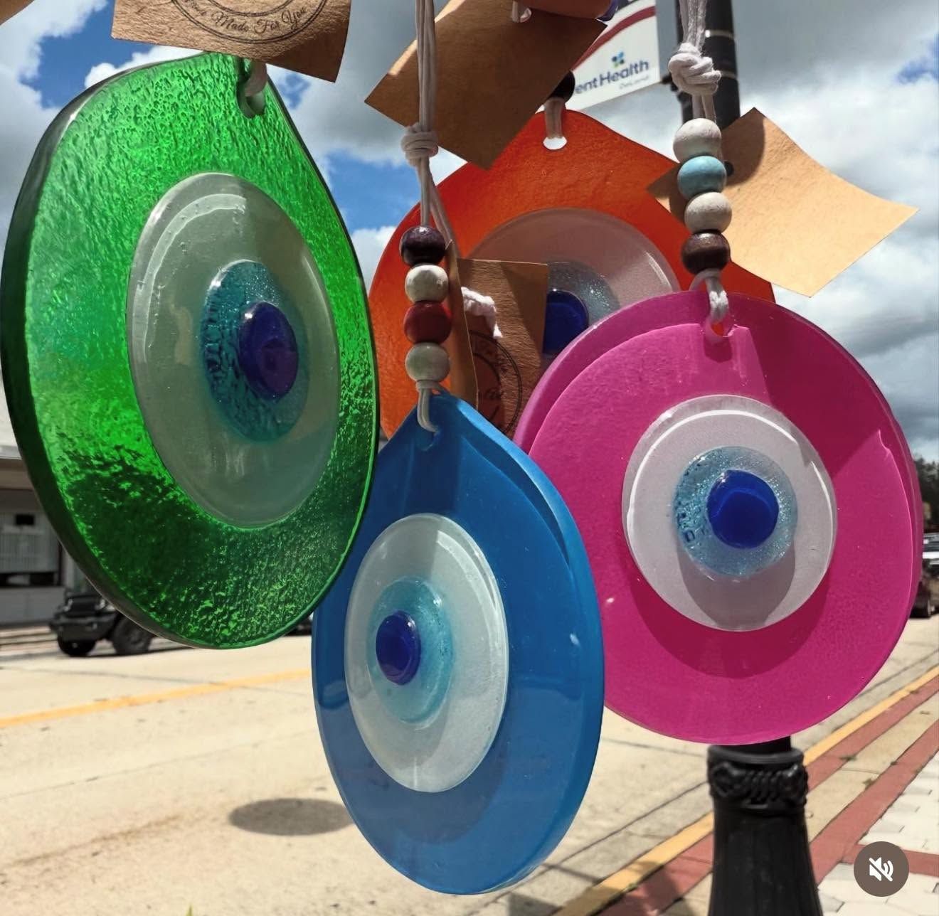 Colorful hanging glass eye ornaments in green, blue, pink, and orange, displayed outdoors.