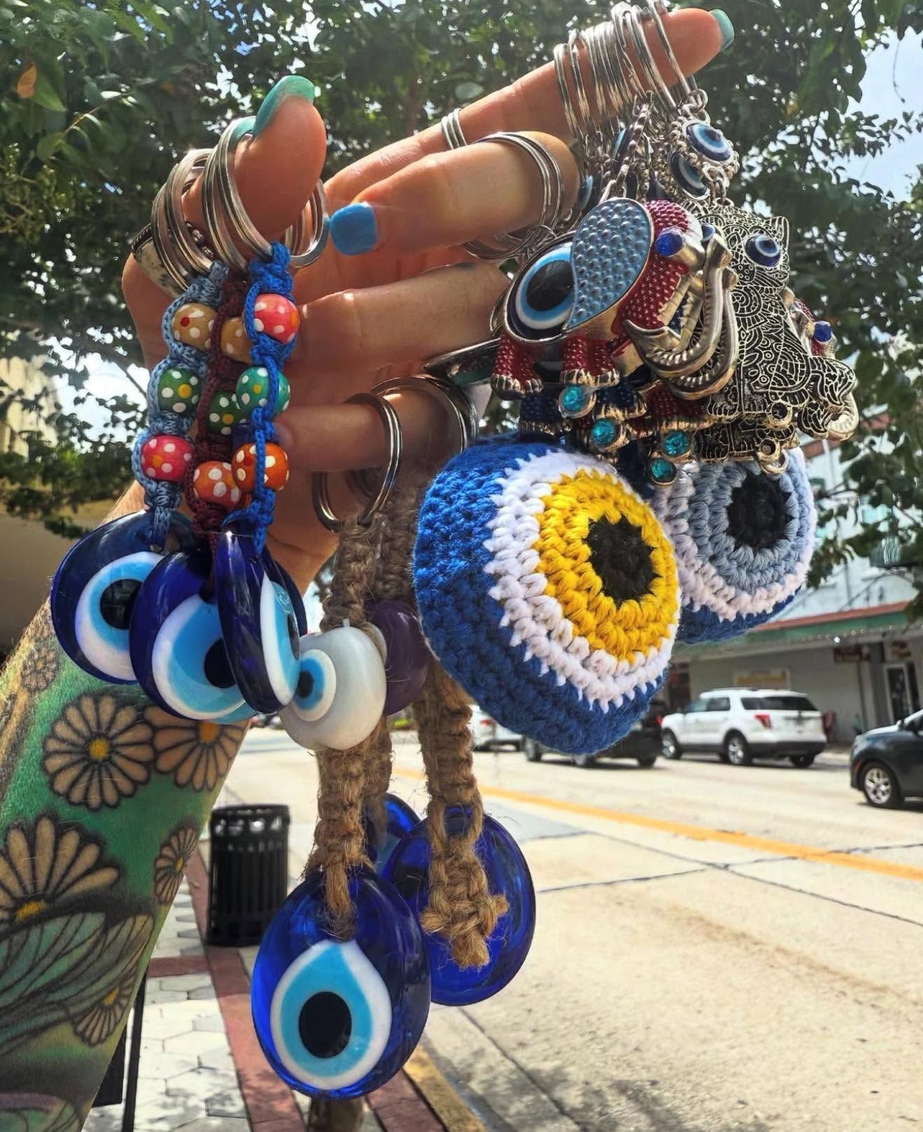 Hand holding colorful beaded eye-shaped earrings and blue evil-eye charms outdoors