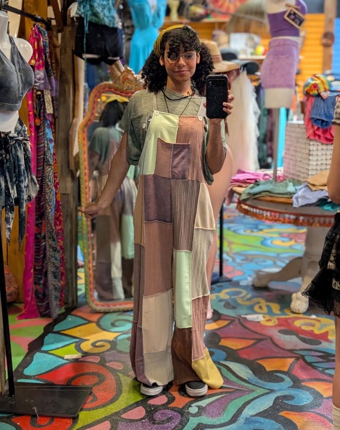 Person posing for a mirror selfie in a colorful clothing store, wearing a patchwork dress.
