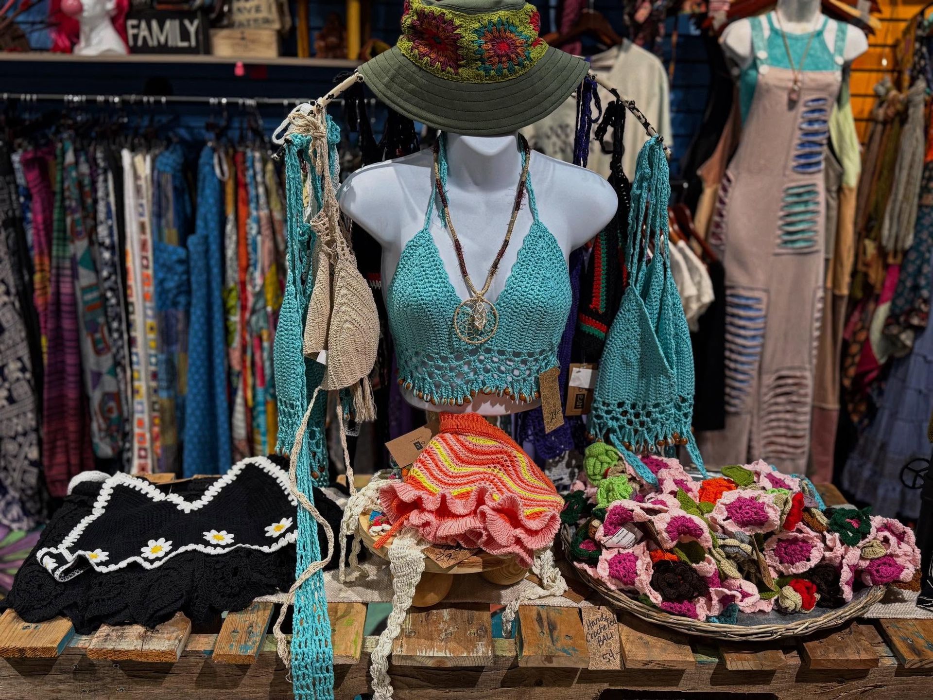 Colorful beachwear display with a turquoise crocheted top, hats, and floral accessories at a market stall