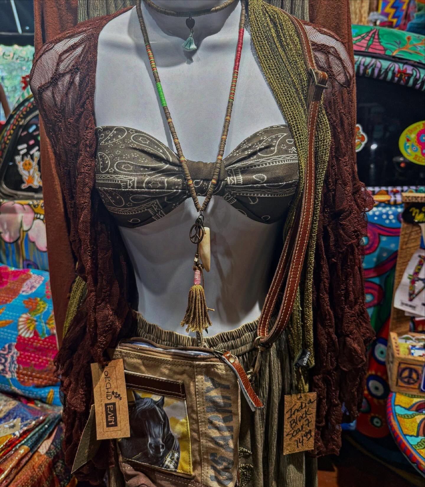 Mannequin wearing a patterned jacket, gold top, layered necklaces, and a metallic bag in a colorful shop display