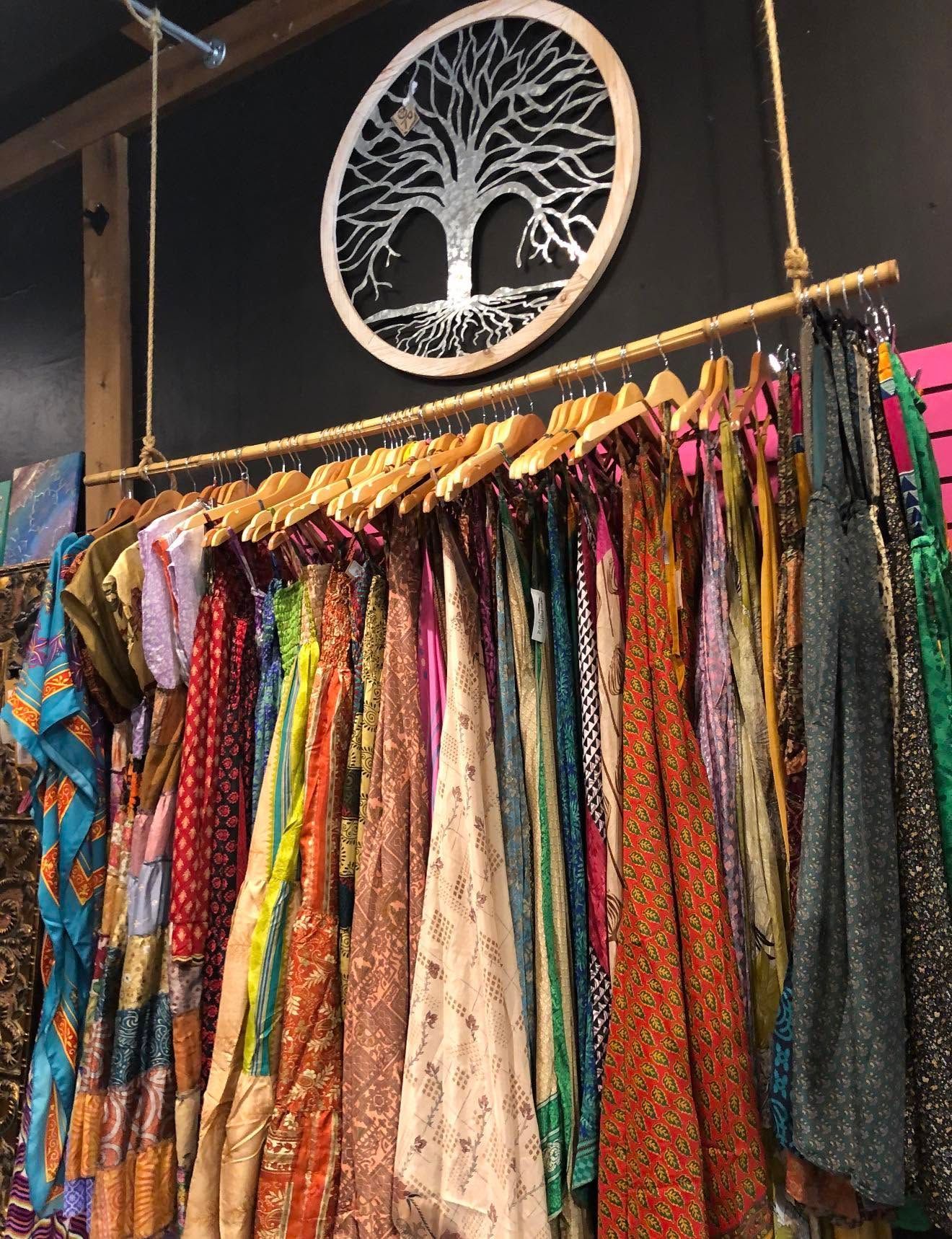 Colorful patterned scarves and fabrics hanging in a shop beneath a decorative tree wall sign