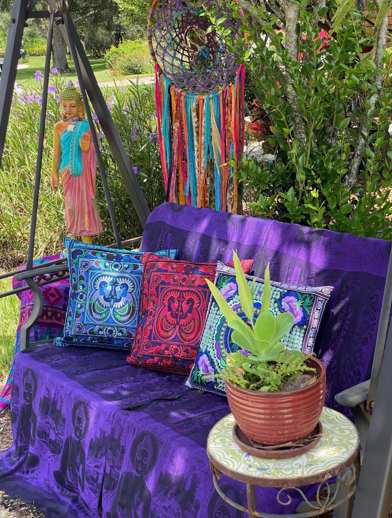 Purple outdoor swing with colorful pillows, a potted plant, and hanging beaded decoration in a garden.