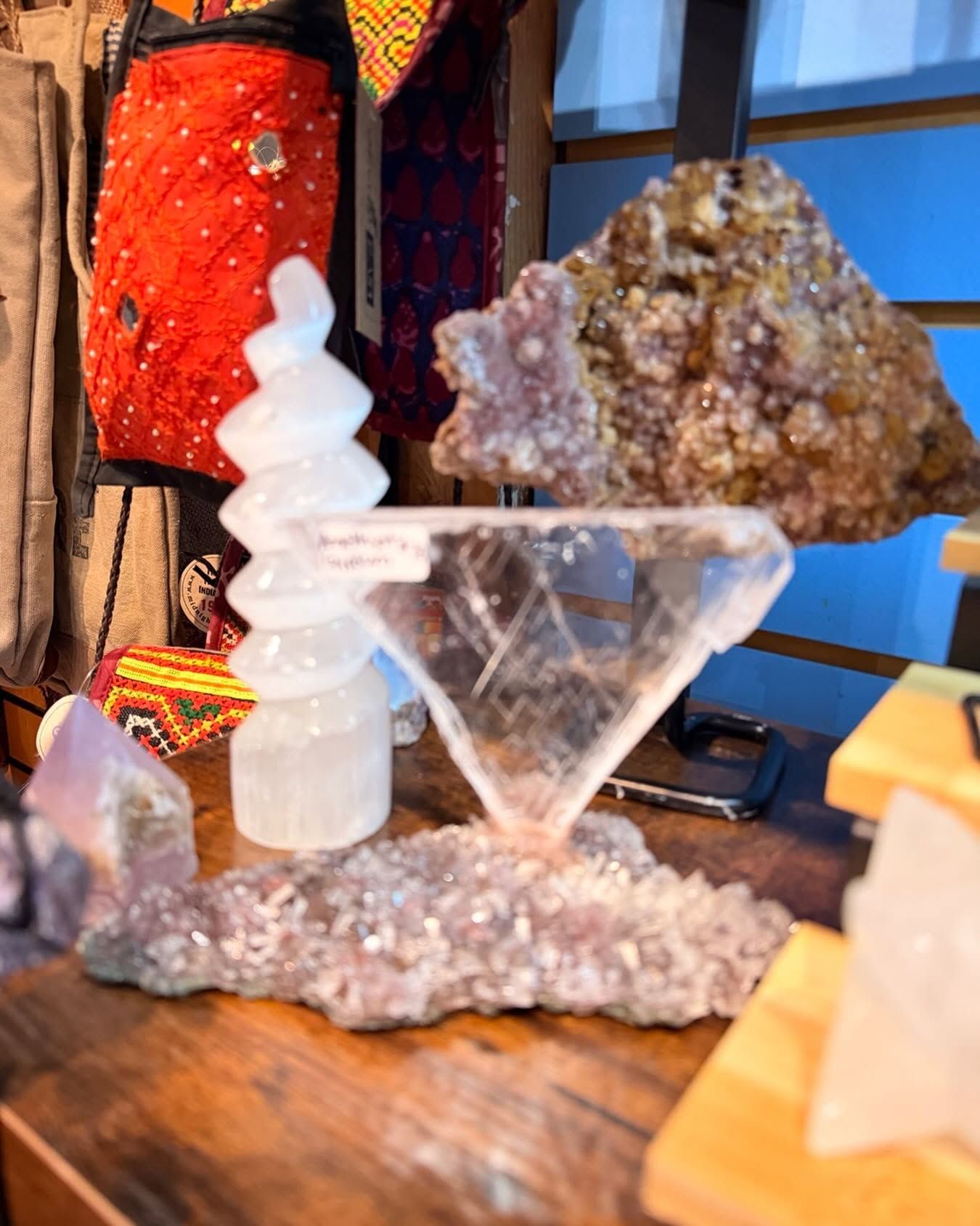Quartz crystal display with a clear spiral tower and small pyramid on a wooden shelf, beside a red lamp.