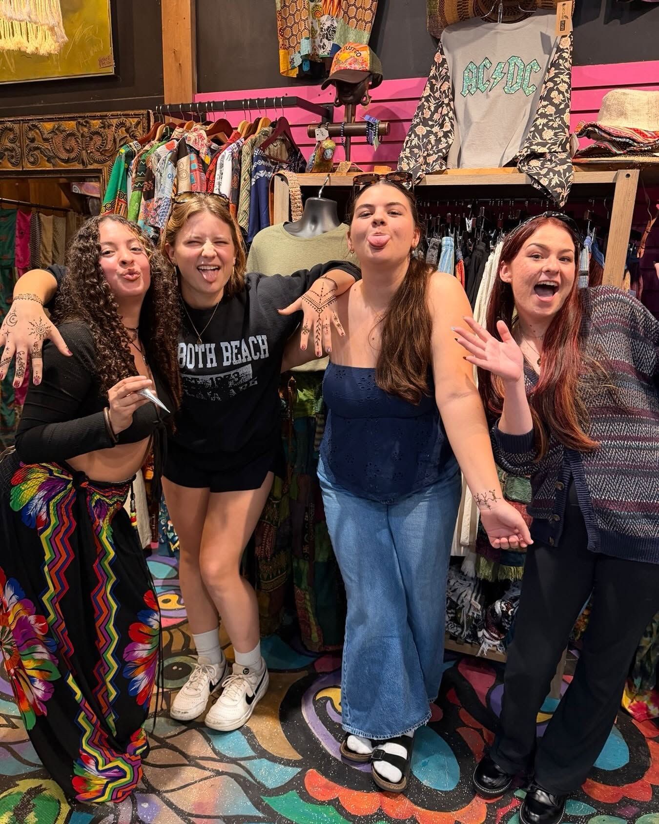 Four friends posing and smiling in a colorful boutique with racks of patterned clothes.