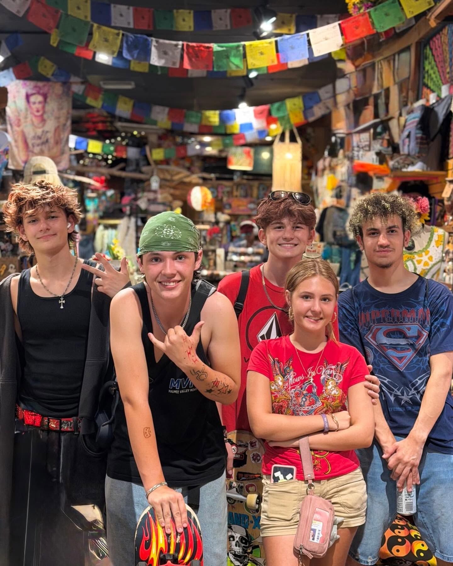 Five smiling people posing in a colorful decorated shop with hanging flags and shelves in the background